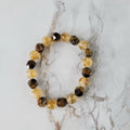 A beaded stretch bracelet featuring faceted brown and amber-yellow gemstone beads, displayed on a white marble surface with gray veining.