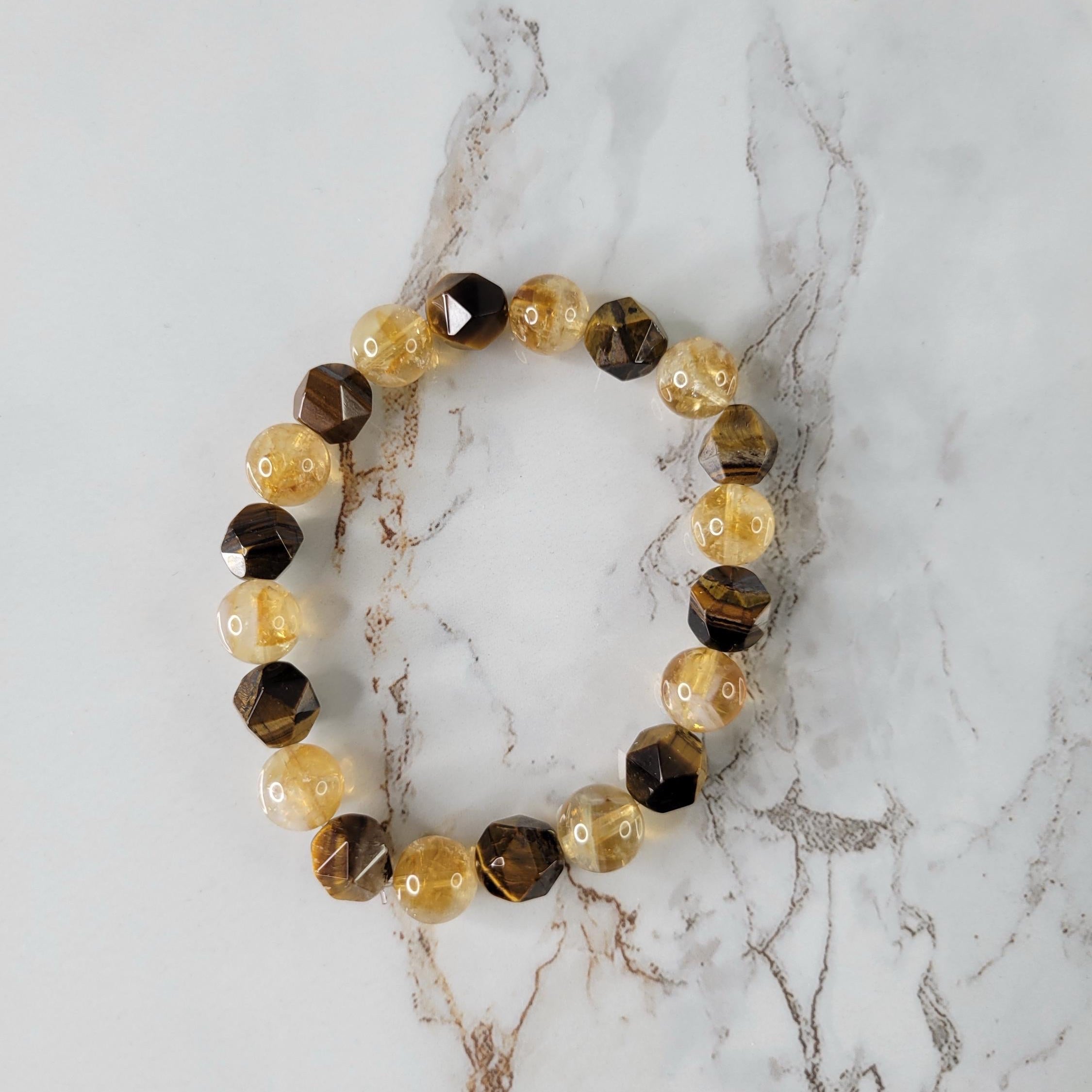 A beaded stretch bracelet featuring faceted brown and amber-yellow gemstone beads, displayed on a white marble surface with gray veining.